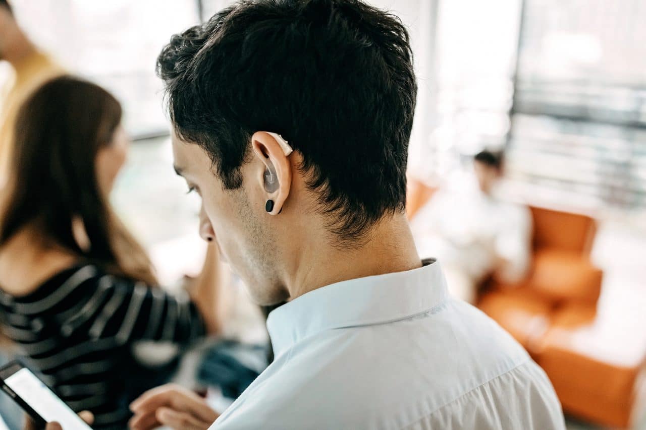 Younger man wearing a hearing aid while using a smartphone.