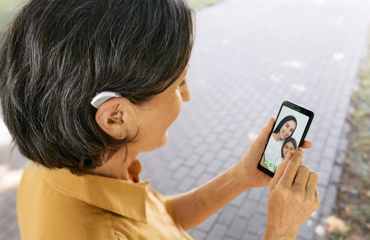 Woman with hearing aid video chatting her granddaughter on her phone.