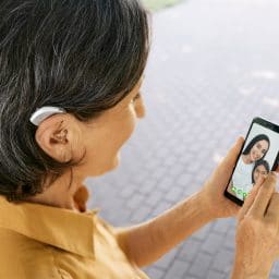 Woman with hearing aid video chatting her granddaughter on her phone.