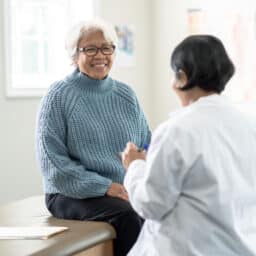 Older woman sitting on the exam table and talking with her primary care provider.