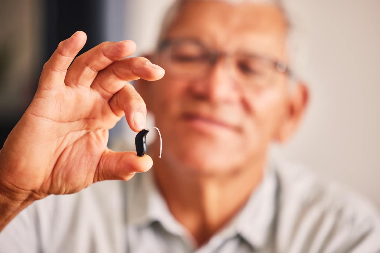 Man holding up a small hearing aid.