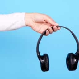 Hand with black wireless headphones on blue background